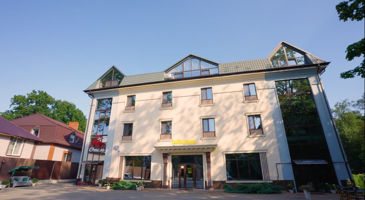 Уютный номер отеля с обеденной зоной, длинным столом, белыми стульями, подвесными светильниками и окнами с видом на сад